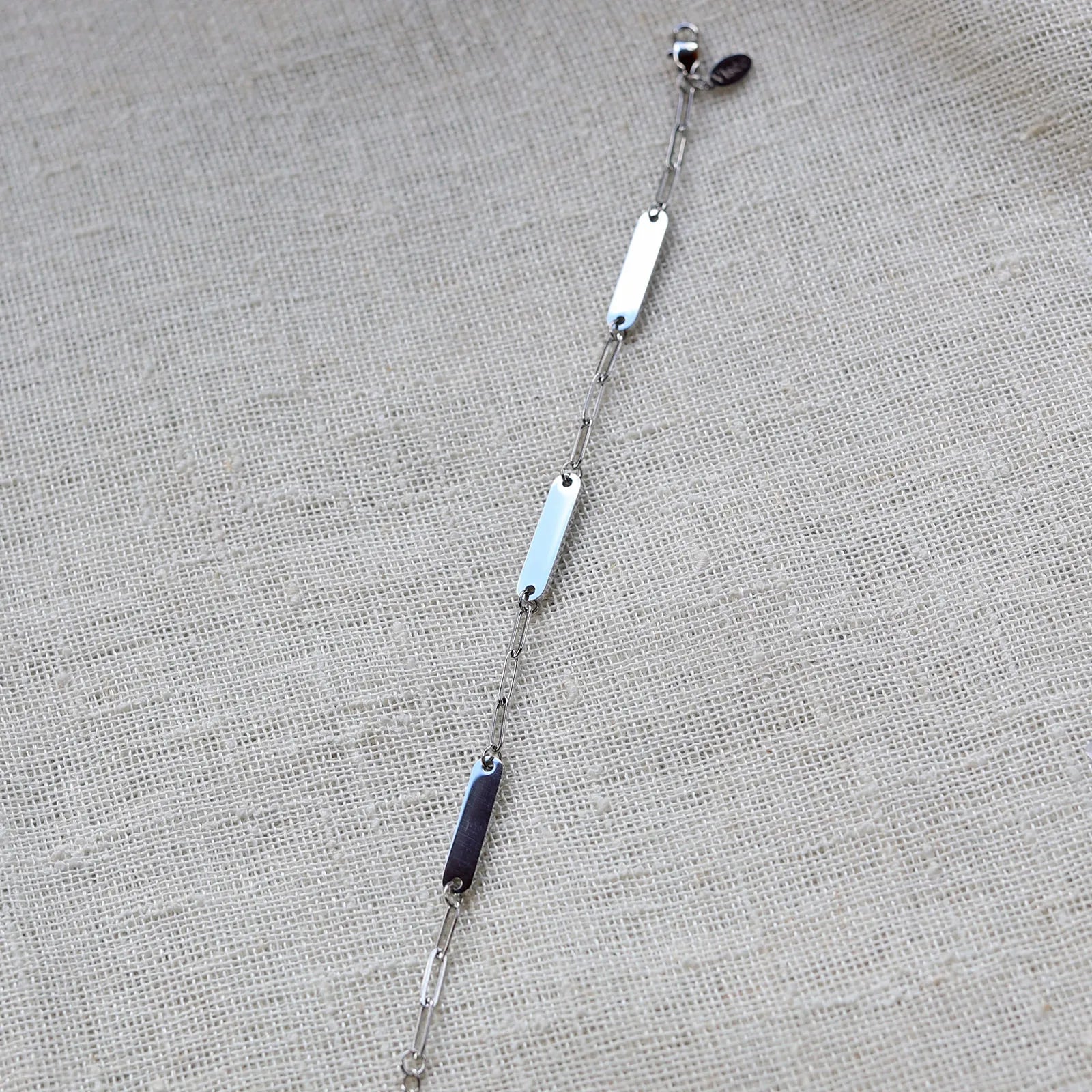 Bracelet "Expression" en acier inoxydable argenté, à personnaliser avec trois plaques gravables, présenté sur un fond beige texturé.