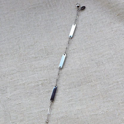 Bracelet "Expression" en acier inoxydable argenté, à personnaliser avec trois plaques gravables, présenté sur un fond beige texturé.