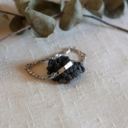 Bracelet "Libère toi" en acier argenté, style gourmette, avec plaque gravable, posé sur un rocher.