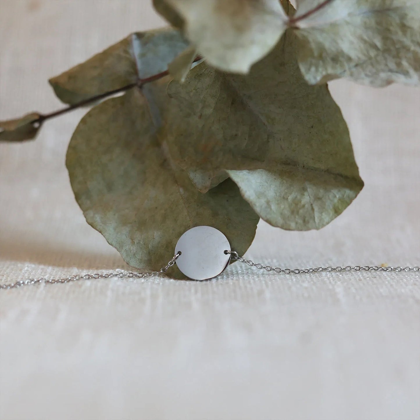 Zoom sur le bracelet "Confiance" en acier argenté personnalisable avec médaille ronde, présenté sur un tissu beige texturé. 