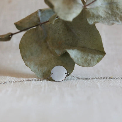 Zoom sur le bracelet "Confiance" en acier argenté personnalisable avec médaille ronde, présenté sur un tissu beige texturé. 