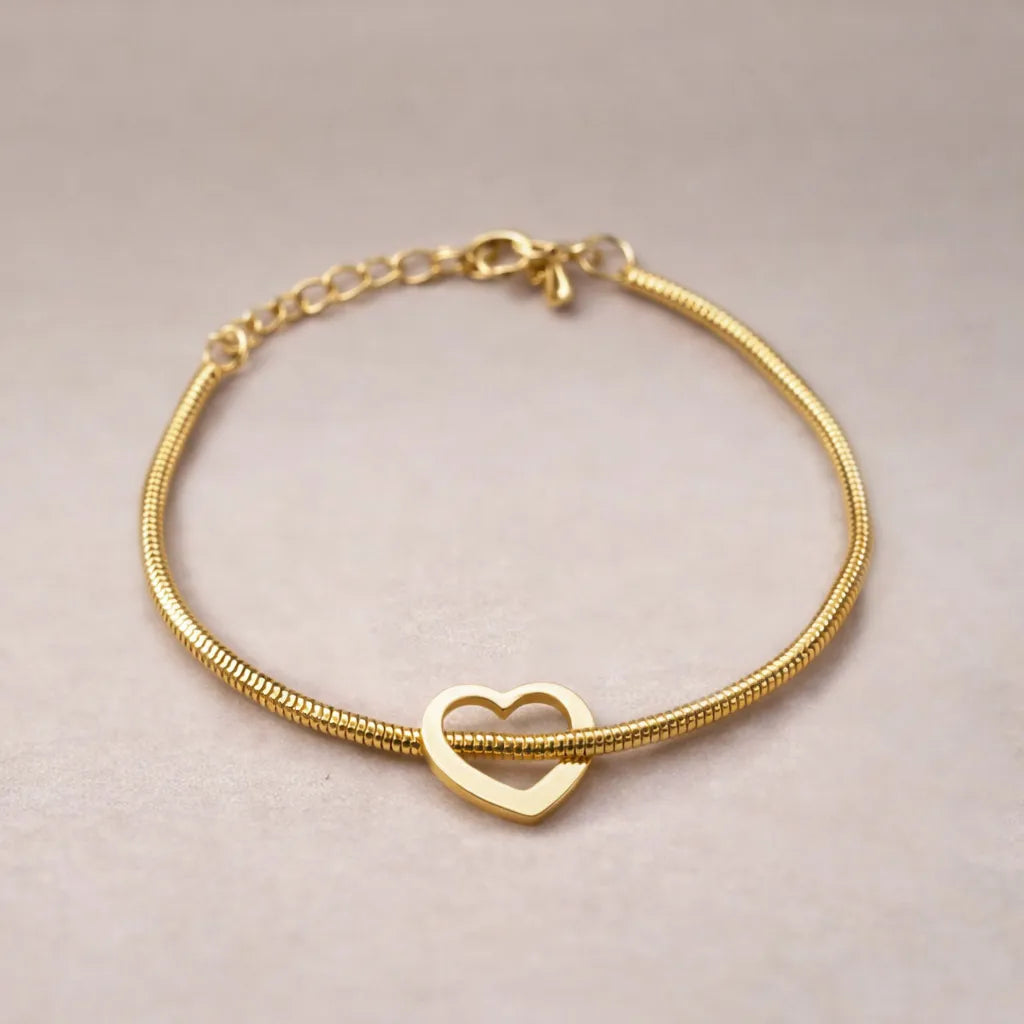 Zoom sur le bracelet "Coeur" en acier doré, orné d'un cœur mobile, posé sur un fond beige texturé.