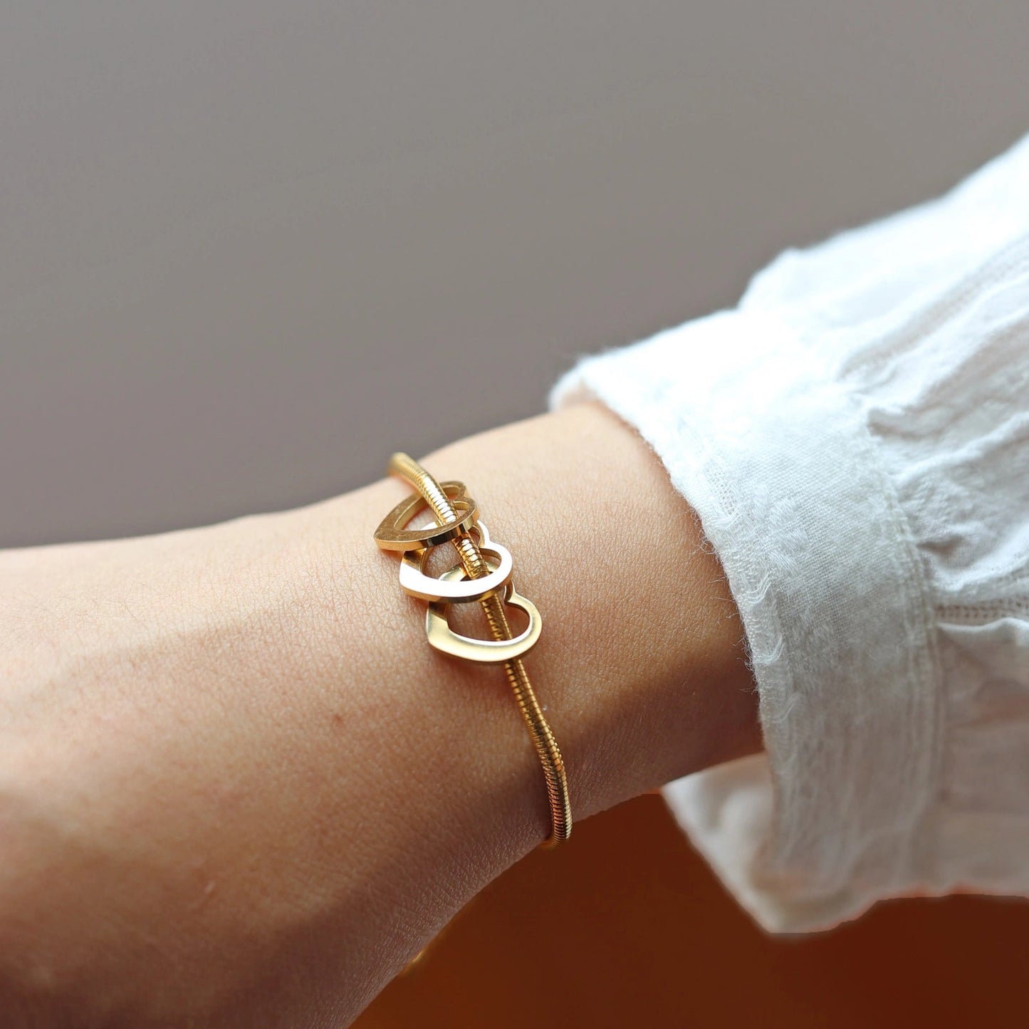 Bracelet "Emotive" en acier doré, orné de trois cœurs mobiles, porté autour du poignet.