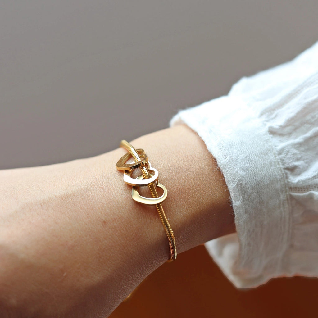 Bracelet "Coeurs" en acier doré, orné de trois cœurs mobiles, porté autour du poignet.