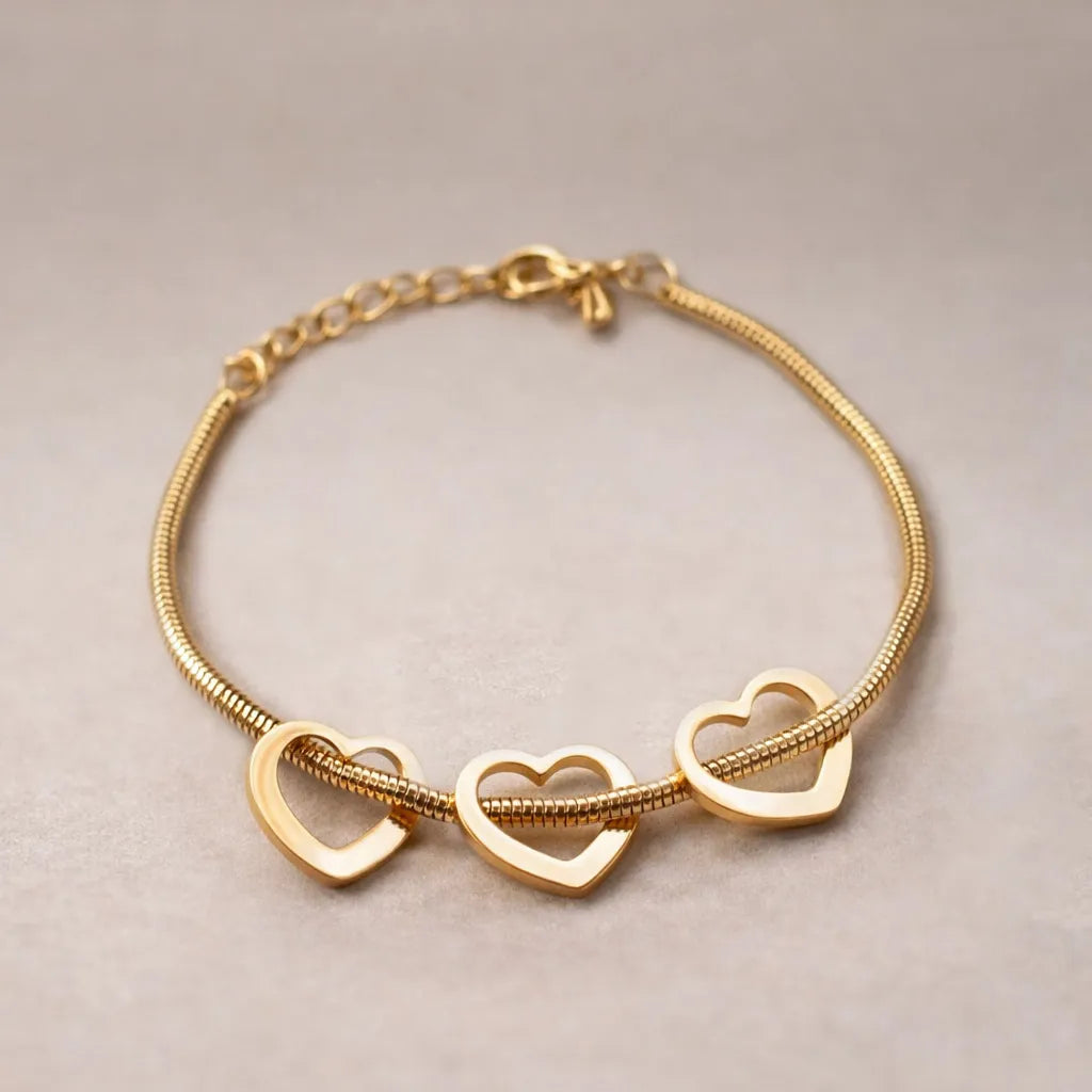 Zoom sur le bracelet "Coeurs en acier doré, orné de trois cœurs mobiles, posé sur un fond beige texturé.