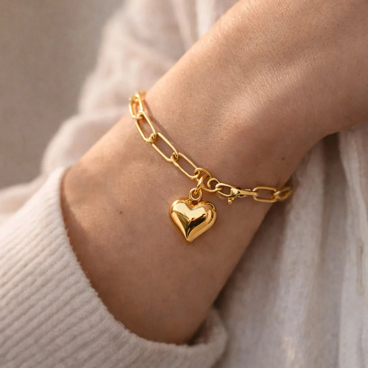 Bracelet Profond en acier inoxydable doré, orné d'une breloque cœur personnalisée, délicatement porté au poignet.