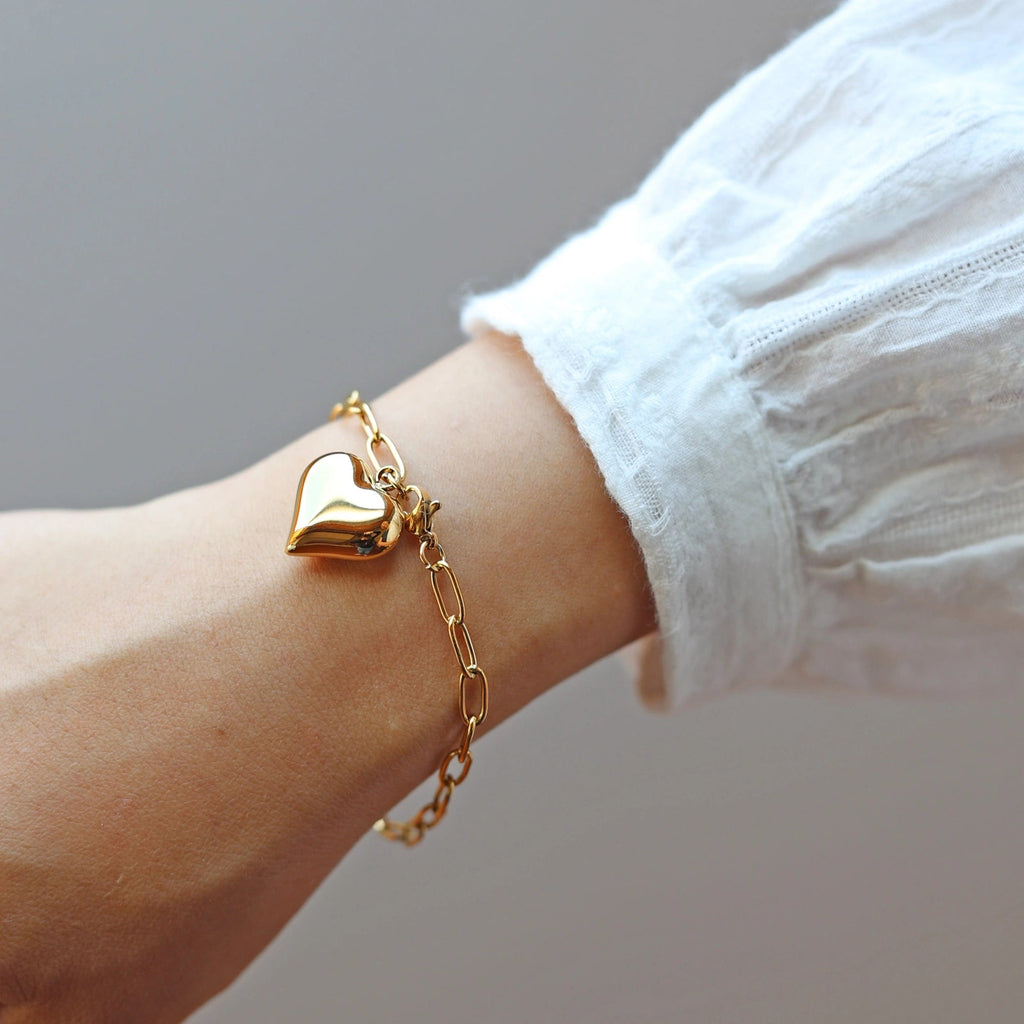 Bracelet Profond en acier inoxydable doré, orné d'une breloque cœur personnalisée, délicatement porté au poignet.