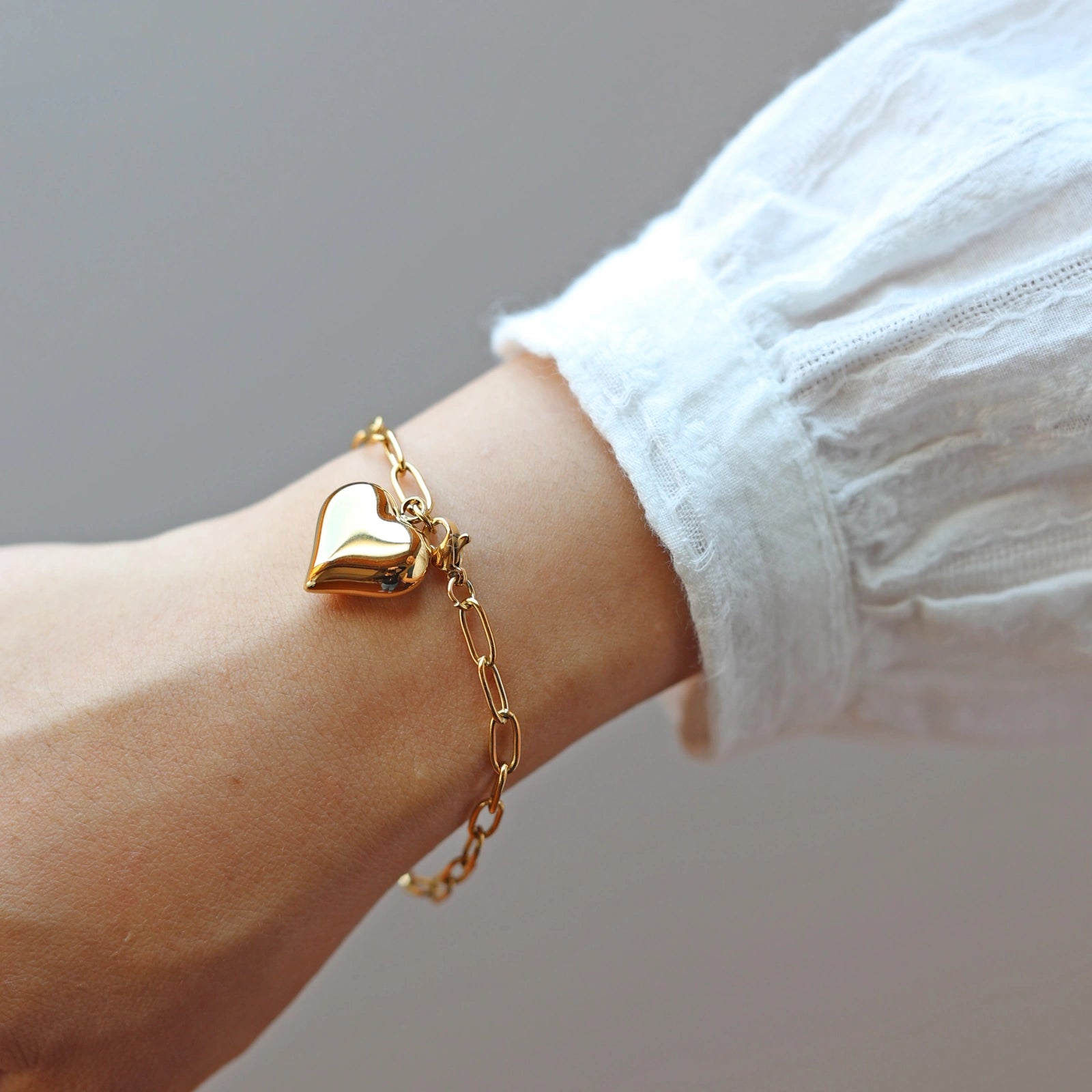 Bracelet Sans filtre en acier inoxydable doré, orné d'une breloque cœur personnalisée, délicatement porté au poignet.