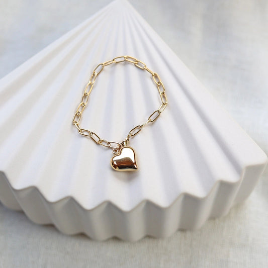 Bracelet Sans filtre en acier inoxydable doré, orné d'une breloque cœur personnalisée , posé sur un fond beige texturé.