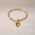 Bracelet Sans filtre en acier inoxydable doré, orné d'une breloque cœur personnalisée, délicatement posé sur un tissu beige