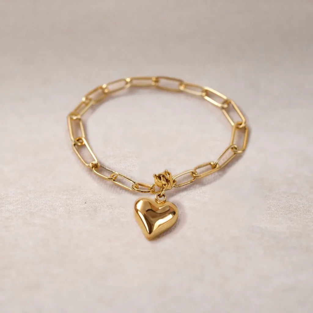 Bracelet Sans filtre en acier inoxydable doré, orné d'une breloque cœur personnalisée, délicatement posé sur un tissu beige