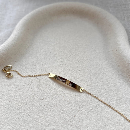 Bracelet gourmette "Sincérité" en acier inoxydable doré,  personnalisé de noms "Thalia Evan", posé sur un fond beige texturé.