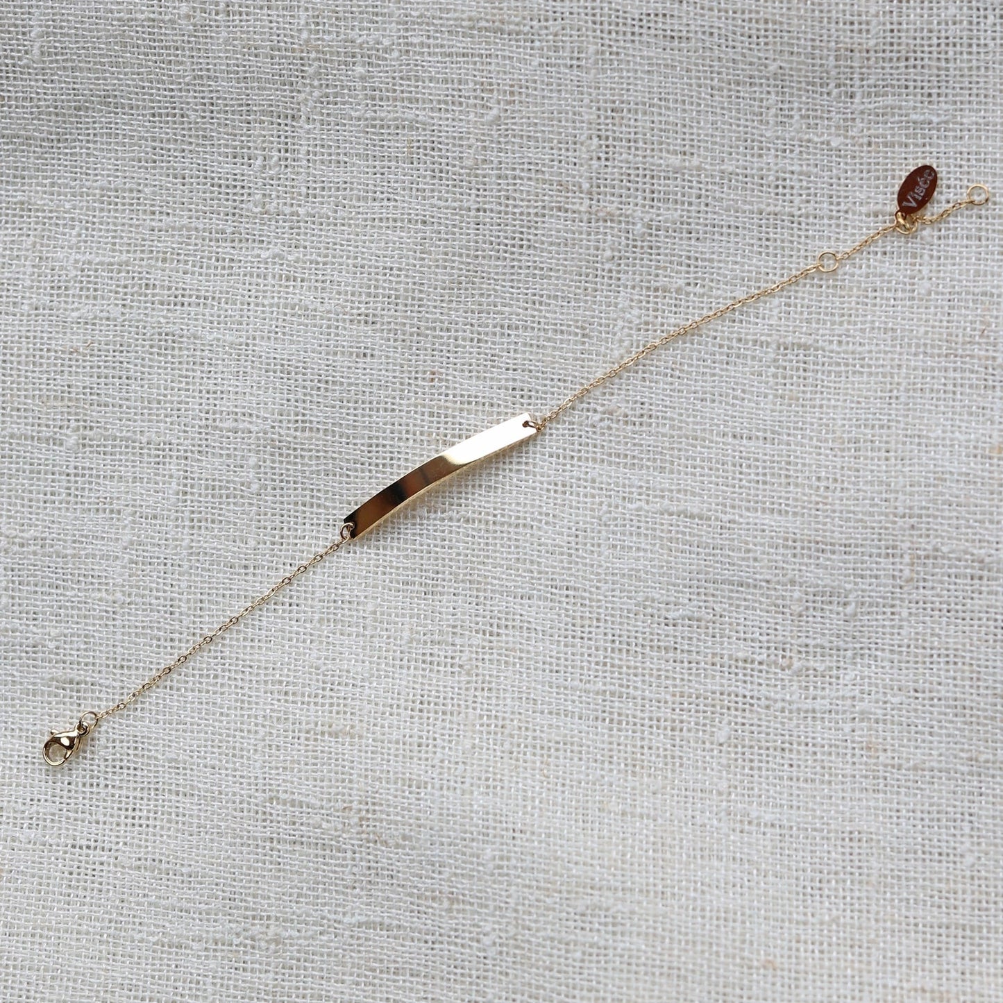 Bracelet gourmette "Sincérité" en acier inoxydable doré,  personnalisable, posé sur un fond beige texturé.