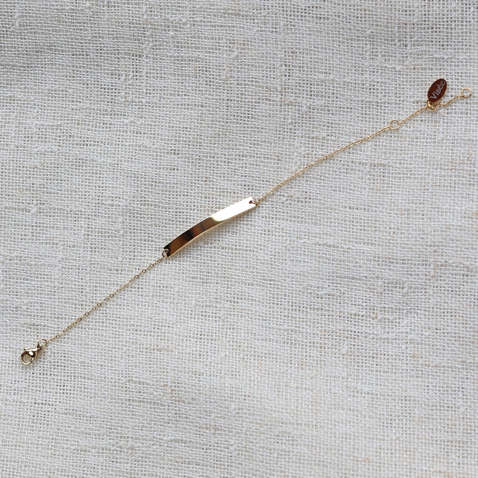 Bracelet gourmette "Sincérité" en acier inoxydable doré,  personnalisable, posé sur un fond beige texturé.