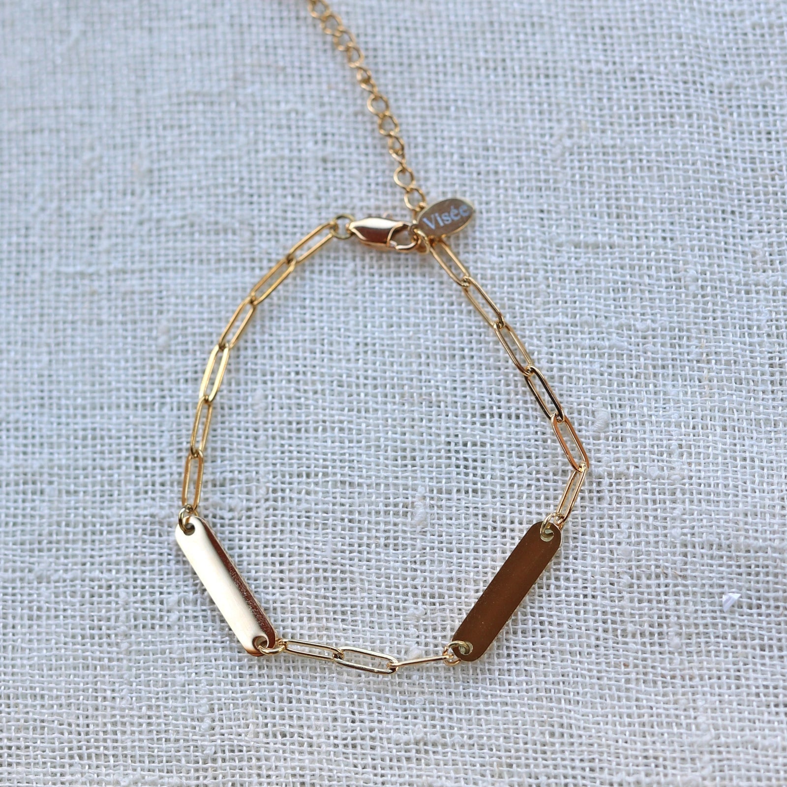 Bracelet "Expression" en acier inoxydable doré, orné de deux plaques personnalisables, présenté sur un fond beige texturé.