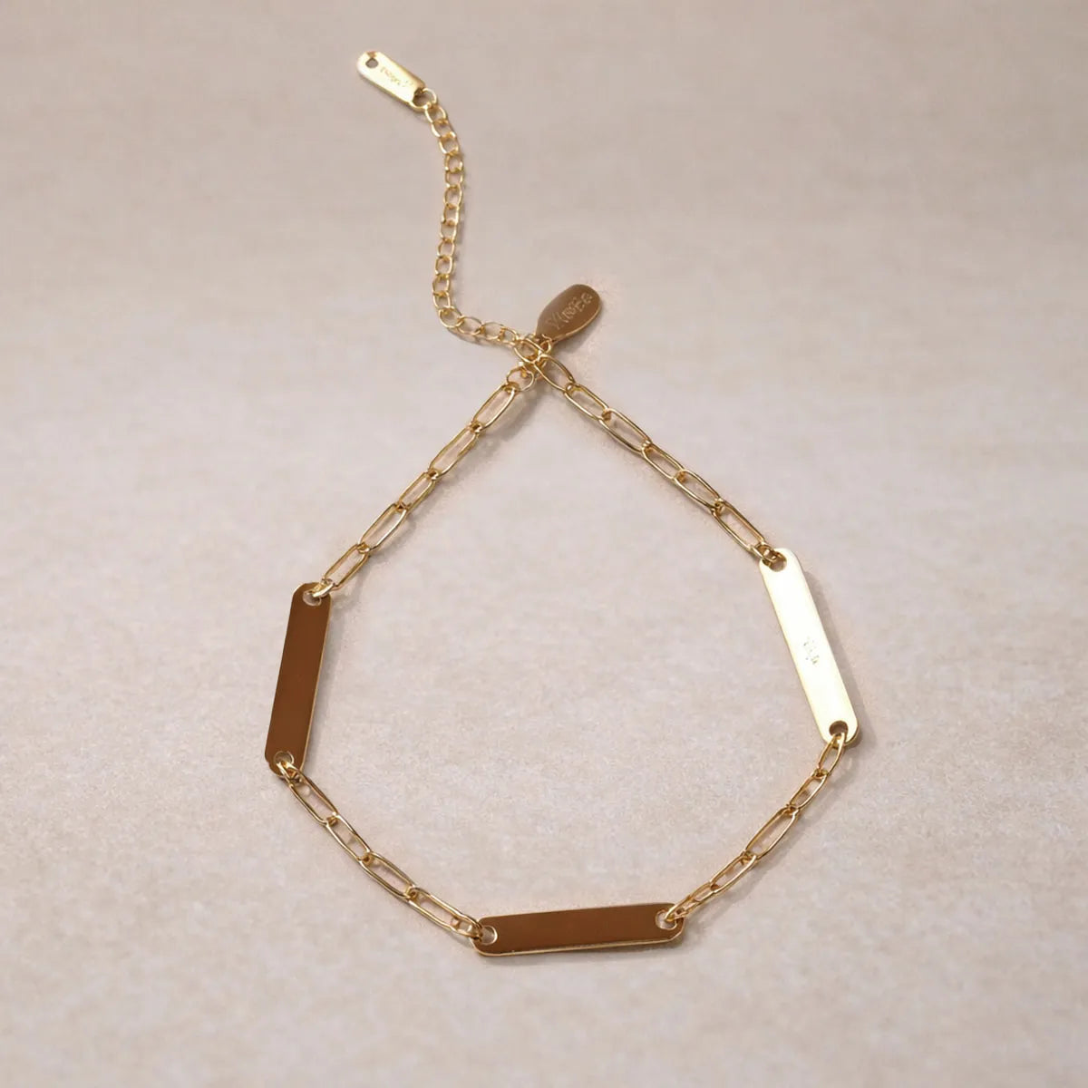 Bracelet 1-2-3 plaques acier doré – Récit Visée Bijoux, posé sur fond beige