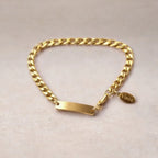 Bracelet "Force" en acier doré, style gourmette, avec plaque gravable, posé sur un fond beige texturé.