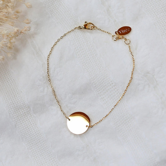 Bracelet "Confiance" en acier doré personnalisable avec médaille ronde, présenté sur un tissu beige texturé. 