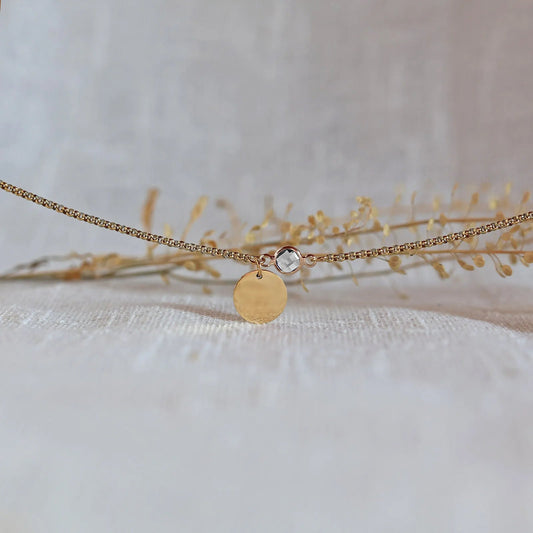 Bracelet "Mon choix" avec médaillon doré personnalisable et pierre blanche, posé sur un fond beige texturé.