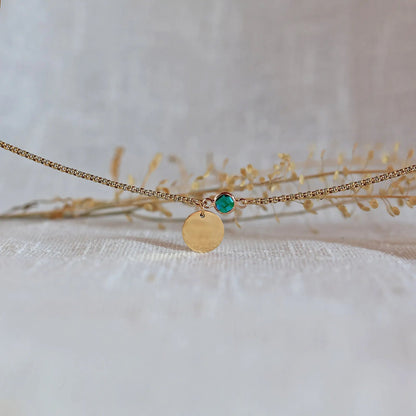 Bracelet "Mon choix" avec médaillon doré personnalisable et pierre vert émeraude, posé sur un fond beige texturé.