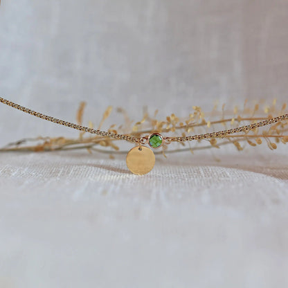 Bracelet "Mon choix" avec médaillon doré personnalisable et pierre vert pomme posé sur un fond beige texturé.