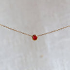 Bracelet "Mon intérieur" en acier doré, orné d'une pierre rouge coulissante personnalisable, posé sur un fond beige.