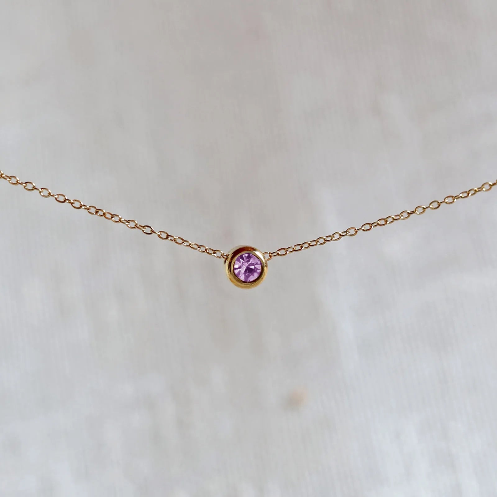 Bracelet "Mon intérieur" en acier doré, orné d'une pierre violette coulissante personnalisable, posé sur un fond beige.