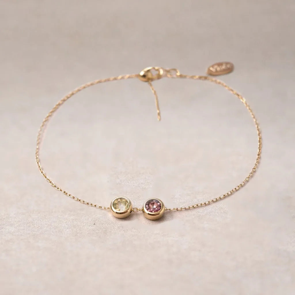 Bracelet "Mon intérieur" en acier doré, orné de pierres de couleurs coulissantes personnalisables, posé sur un fond beige texturé.