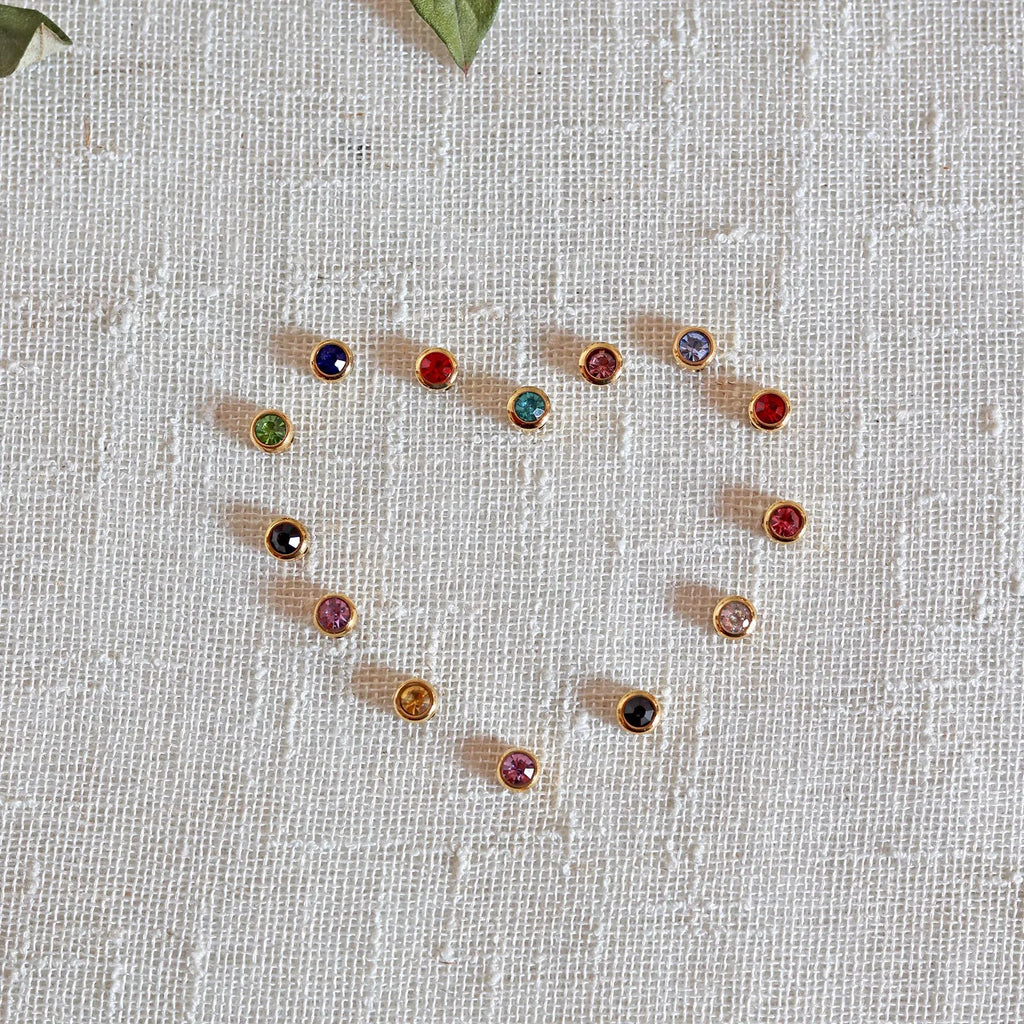 Pierres colorées en acier doré formant un coeur, posées sur un fond beige texturé.