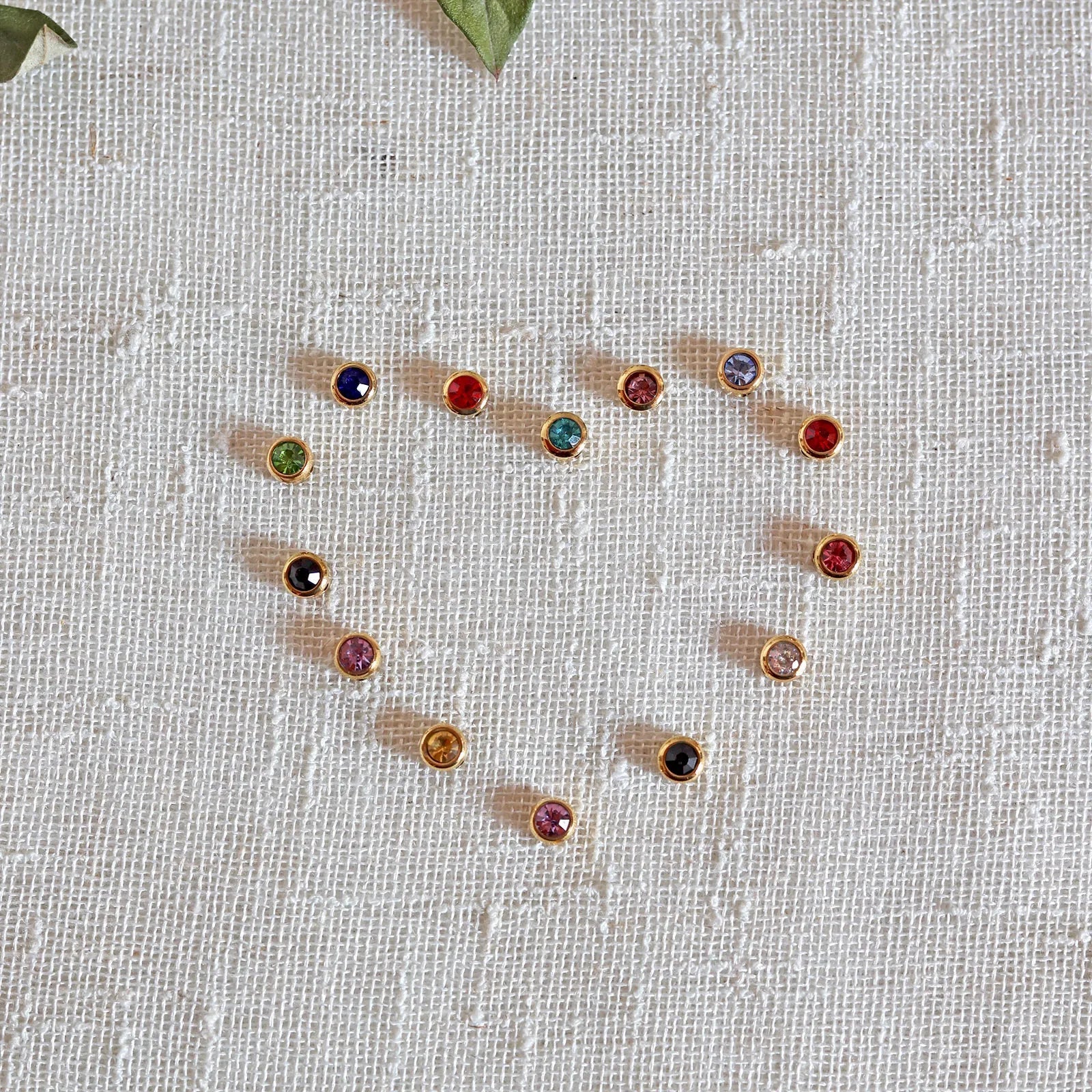Pierres colorées en acier doré formant un coeur, posées sur un fond beige texturé.