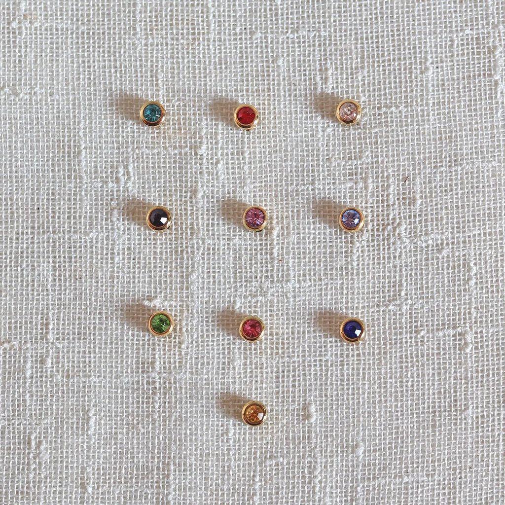 Pierres colorées en acier doré, posées sur un fond beige texturé.