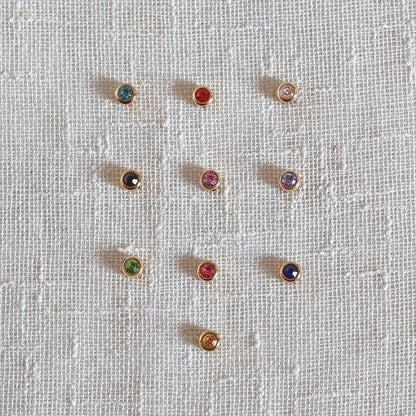 Pierres colorées en acier doré, posées sur un fond beige texturé.