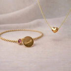 Coffret Signature – Bracelet personnalisé: gravé au prénom Camille et couleur de naissance rose & collier cœur Visée Bijoux, posé sur un fond beige texturé.