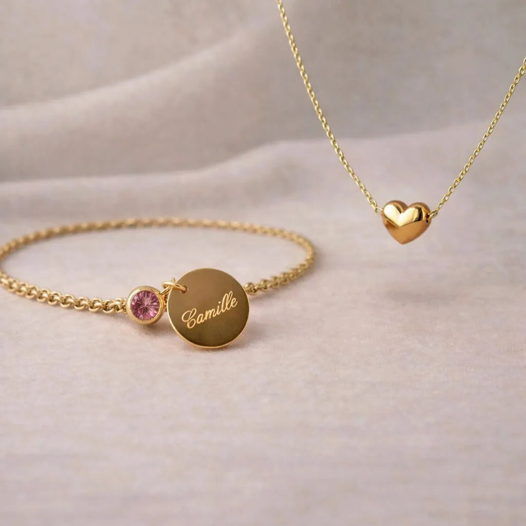 Coffret Signature – Bracelet personnalisé: gravé au prénom Camille et couleur de naissance rose & collier cœur Visée Bijoux, posé sur un fond beige texturé.
