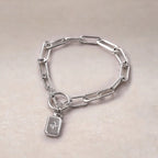 Zoom sur le bracelet Voeu en acier argenté avec breloque rectangulaire personnalisable vue de dos, posé sur un fond beige texturé.