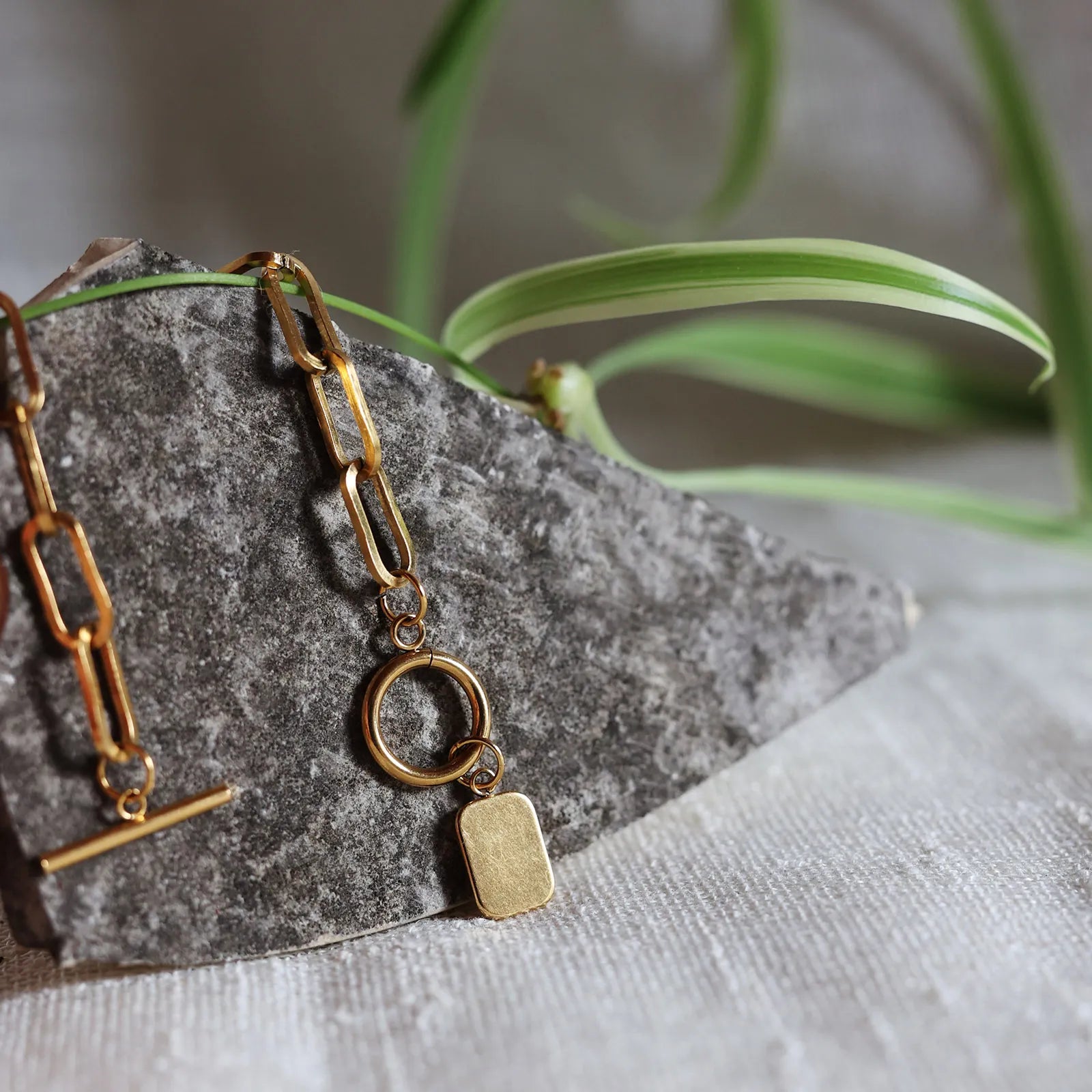 Zoom sur la breloque rectangulaire personnalisable en acier doré de dos, posé sur une pierre granite avec une feuille