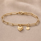 Bracelet Attache  avec breloque cœur à graver avec une initiale en acier inoxydable doré, posé sur un fond beige texturé.