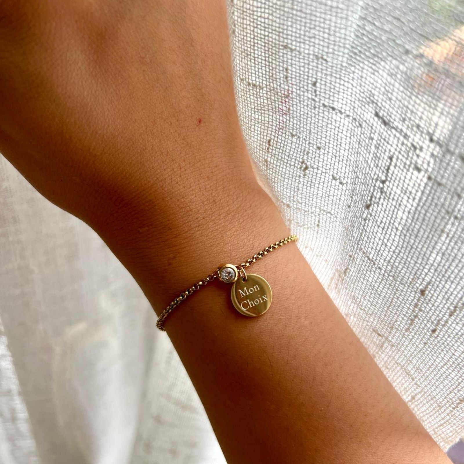 Bracelet Mon choix doré, bijou personnalisable en acier inoxydable avec médaillon gravé "Mon choix" et pierre de naissance blanche, porté au poignet.