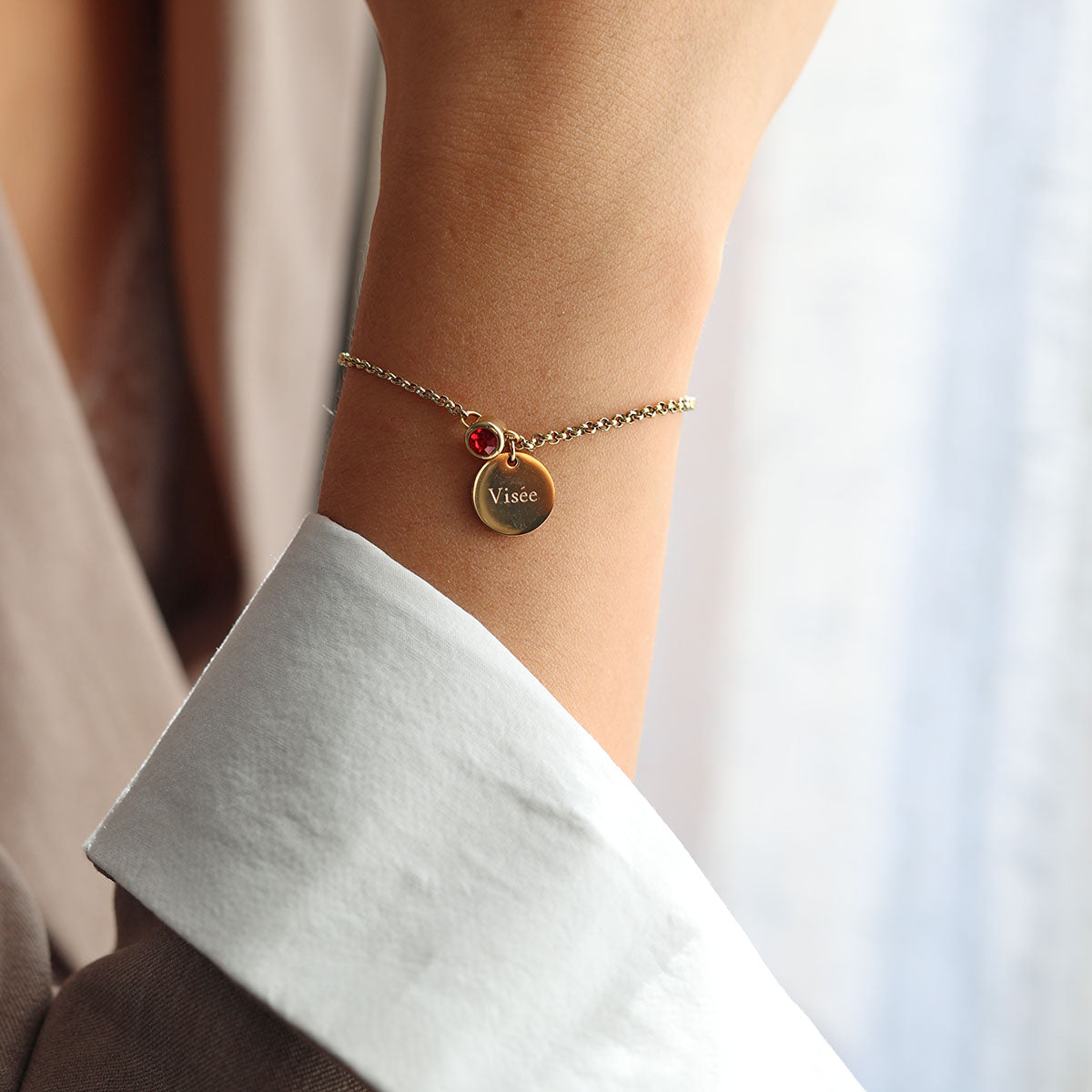 Bracelet Mon choix doré, bijou personnalisable en acier inoxydable avec médaillon gravé "Visée" et pierre de naissance rouge, porté au poignet.