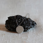 Collier "Reflet" avec médaille ronde personnalisé en acier inoxydable argenté, personnalisé LIBRE, posé sur une pierre noire volcanique
