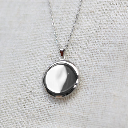 Gros plan sur le collier "Ce jour là" avec médaillon rond personnalisable en acier argenté, présenté sur un fond beige texturé.