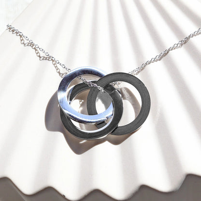 Zoom sur le collier "Je deviens" en acier argenté, avec trois cercles entrelacés personnalisables, posé sur un fond beige texturé.