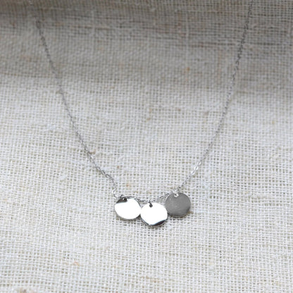 Collier "Inspiration" en acier inoxydable argenté, composé de trois médaillons personnalisables, présenté sur un fond beige texturé.