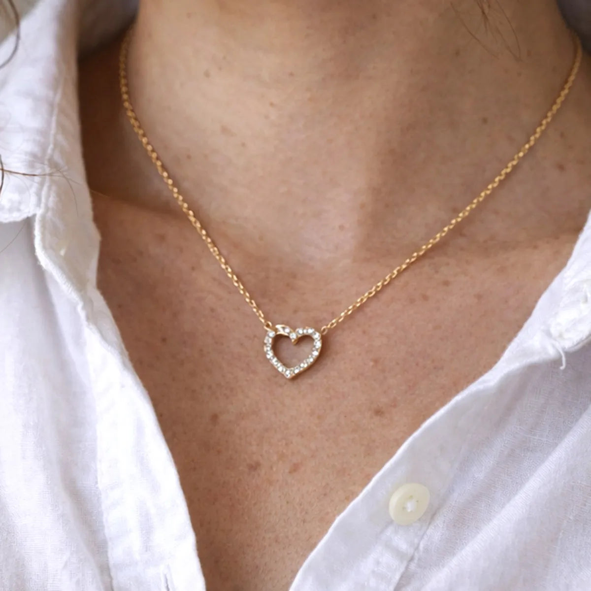 Collier Sentiment, avec pendentif cœur serti de brillants en acier inoxydable doré, porté autour du cou. 