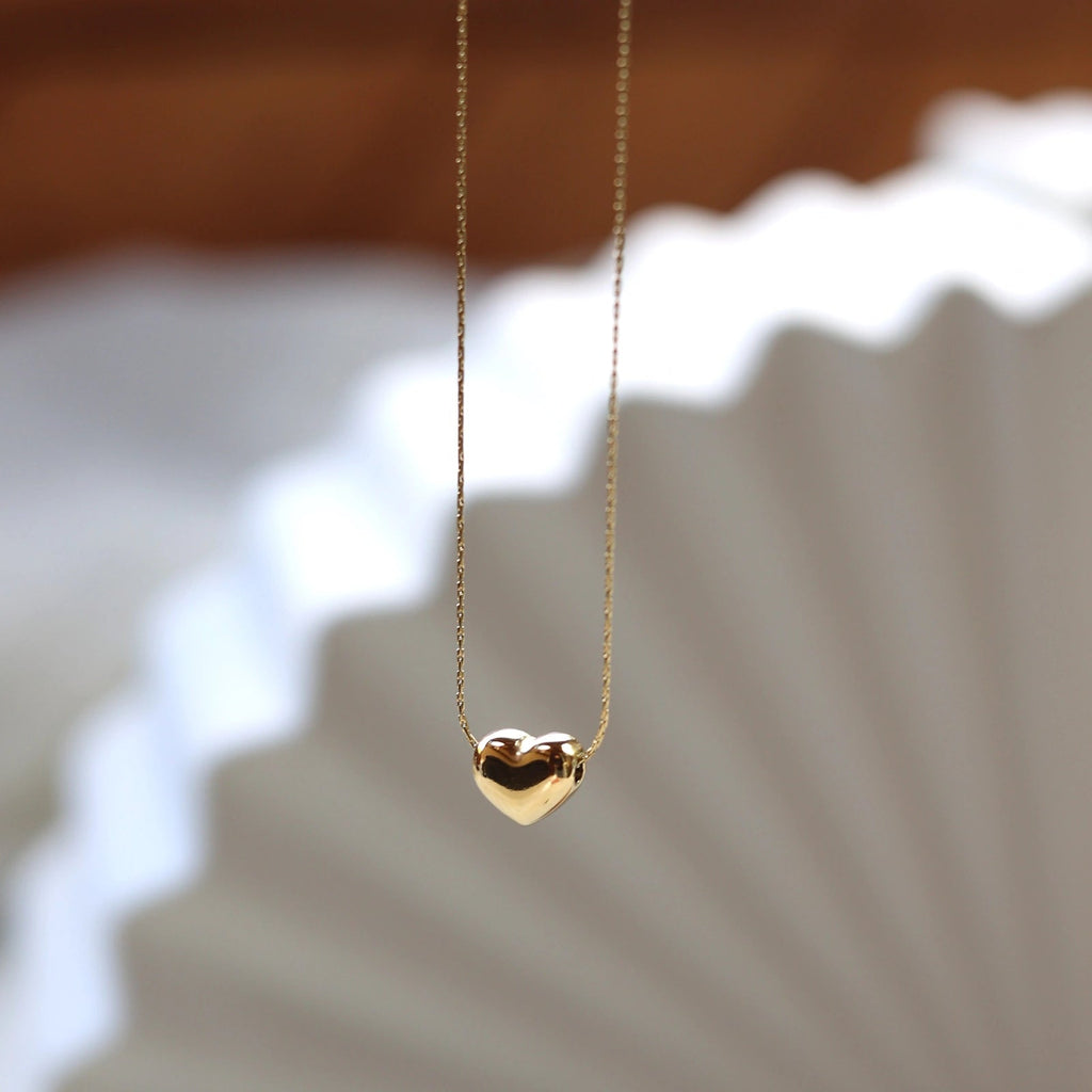 Collier Authentique, avec pendentif cœur personnalisable, en acier inoxydable doré, photographié en vue d'ensemble sur un fond beige texturé.