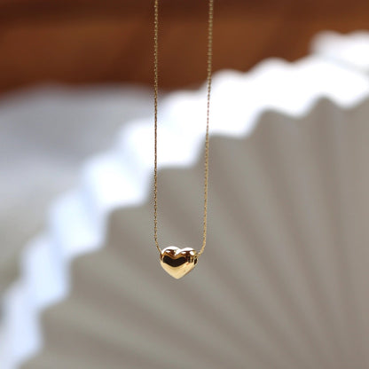 Collier Authentique, avec pendentif cœur personnalisable, en acier inoxydable doré, photographié en vue d'ensemble sur un fond beige texturé.
