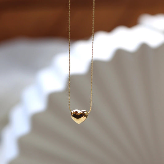 Collier Authentique, avec pendentif cœur personnalisable, en acier inoxydable doré, photographié en vue d'ensemble sur un fond beige texturé.
