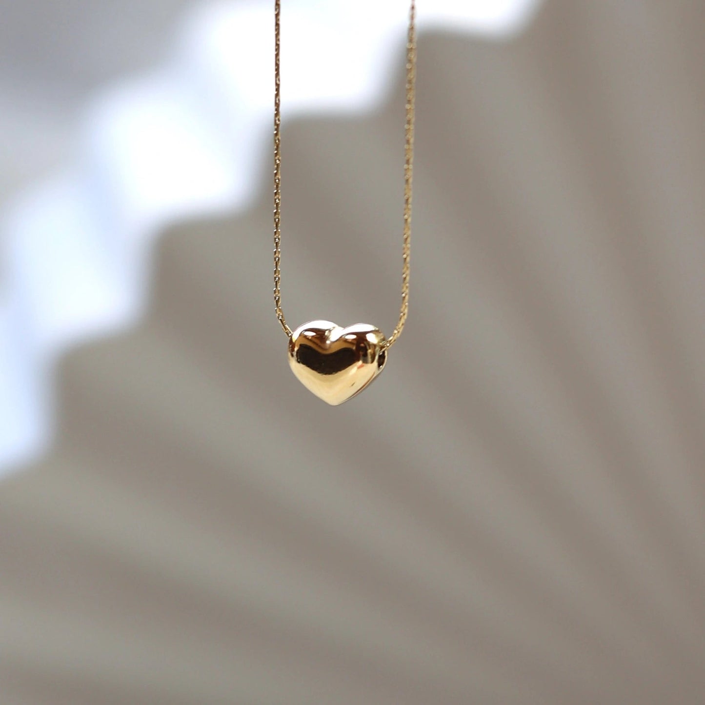 Collier Authentique avec pendentif cœur personnalisable, en acier inoxydable doré, photographié en gros plan sur un fond beige texturé.