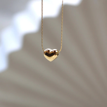 Collier Authentique avec pendentif cœur personnalisable, en acier inoxydable doré, photographié en gros plan sur un fond beige texturé.