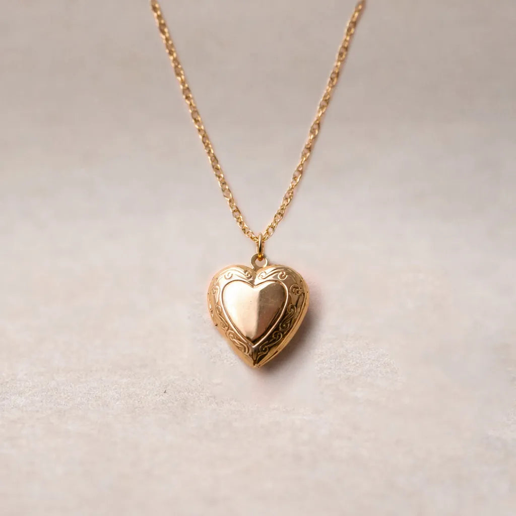 Zoom sur le collier "Entre nous", médaillon cœur en acier doré avec photo souvenir à personnaliser, posé sur un fond beige texturé.